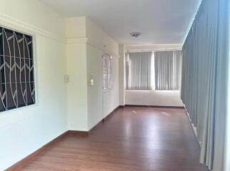 Empty living room with wooden flooring, windows with vertical blinds, and white walls