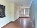 Empty living room with wooden flooring, windows with vertical blinds, and white walls