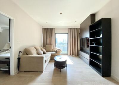 Modern living room with beige sofas, a coffee table, built-in shelves, and a wall-mounted TV, featuring natural light from large windows with beige curtains.