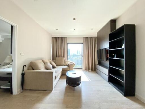 Modern living room with beige sofas, a coffee table, built-in shelves, and a wall-mounted TV, featuring natural light from large windows with beige curtains.