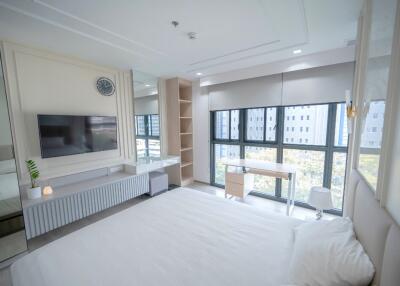 Modern bedroom with large windows, TV, bed, and study desk