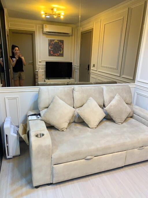 Living room with light-beige couch, wall-mounted TV, and air conditioning unit