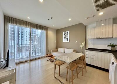 Modern living room with light wood flooring, large windows, and a small dining area