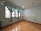 Empty bedroom with wooden flooring and large window with curtains