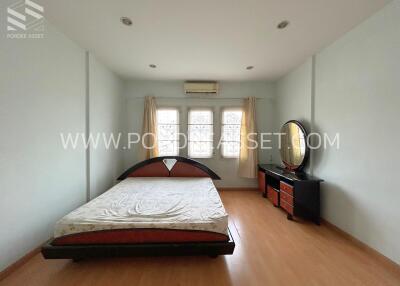 Spacious bedroom with a large bed, chest of drawers with a mirror, and three windows.