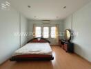 Spacious bedroom with a large bed, chest of drawers with a mirror, and three windows.