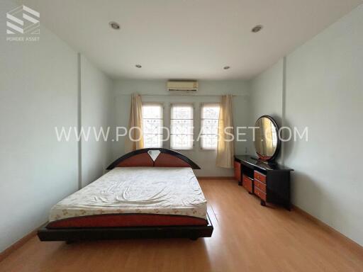 Spacious bedroom with a large bed, chest of drawers with a mirror, and three windows.