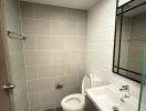 Modern bathroom with tiled walls and floor, sink, toilet, and mirror.