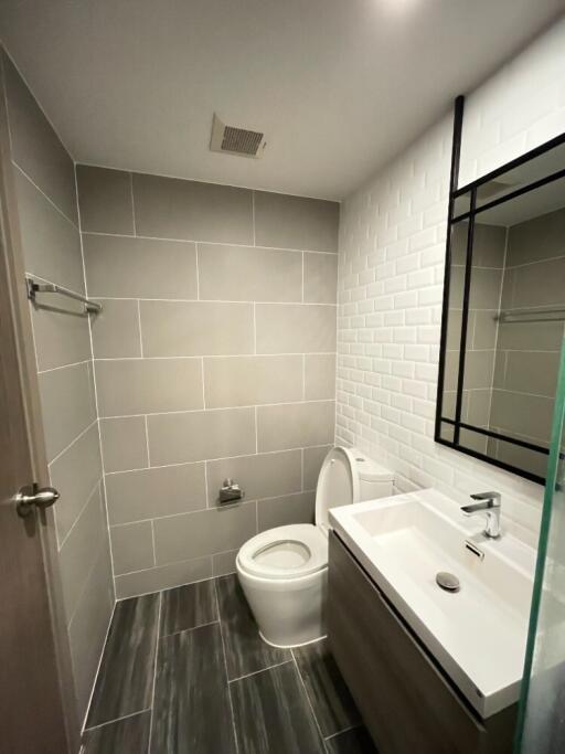 Modern bathroom with tiled walls and floor, sink, toilet, and mirror.