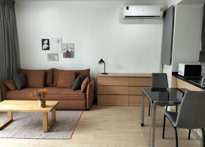 Modern living room with a brown sofa, wooden coffee table, wall-mounted air conditioner, and dining area.