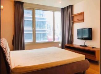 A bedroom with a large window, bed, wall-mounted television, and shelves.