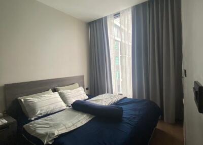 Cozy bedroom with a double bed, side table, and large window with gray curtains