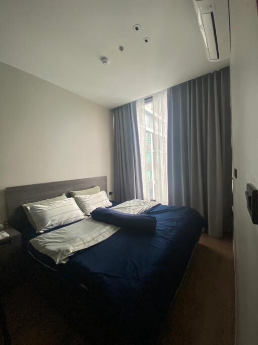 Cozy bedroom with a double bed, side table, and large window with gray curtains