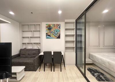 Modern living area with sofa, dining table, and glass partition leading to bedroom