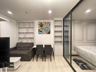 Modern living area with sofa, dining table, and glass partition leading to bedroom