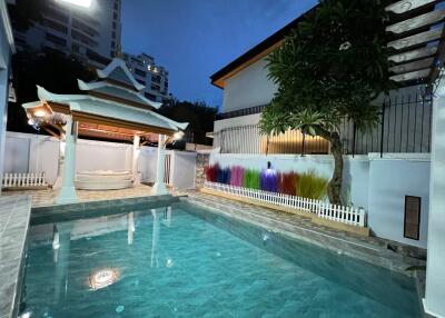 Outdoor view of a swimming pool at dusk, with a gazebo and surrounding decorations.