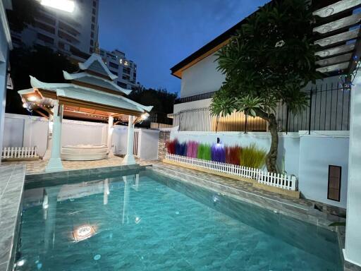 Outdoor view of a swimming pool at dusk, with a gazebo and surrounding decorations.