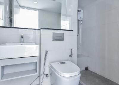 Modern bathroom with a sleek design, featuring a toilet, washbasin, large mirror, and shower area