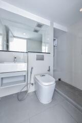 Modern bathroom with a sleek design, featuring a toilet, washbasin, large mirror, and shower area