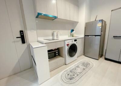 Modern kitchen with white cabinets, a washing machine, microwave, fridge, and a countertop for appliances.