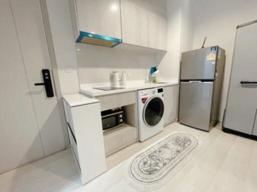 Modern kitchen with white cabinets, a washing machine, microwave, fridge, and a countertop for appliances.