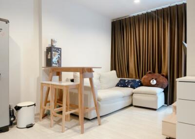 Modern living room with a white sofa, wooden table, stools, and floor-length curtains