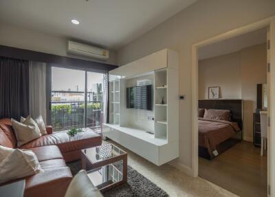 Modern living room with leather couch and wall-mounted TV unit adjacent to a bedroom