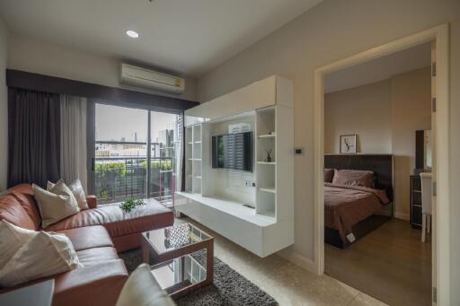 Modern living room with leather couch and wall-mounted TV unit adjacent to a bedroom