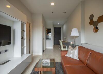 Modern living room with brown leather couch, glass coffee table, TV, and wall decor