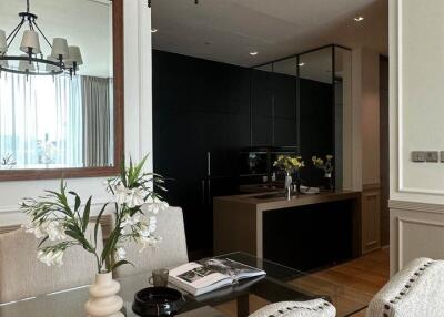 Elegant dining area with glass table, stylish chandelier, and modern kitchen in the background