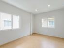 Empty bedroom with wooden flooring and two large windows