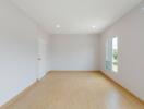 Spacious empty bedroom with wooden flooring and white walls