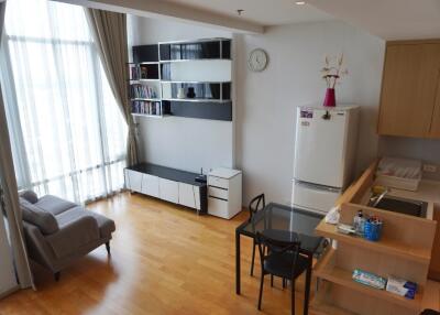 Modern living area with large window, wooden floor, shelves, and kitchen corner