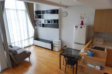 Modern living area with large window, wooden floor, shelves, and kitchen corner