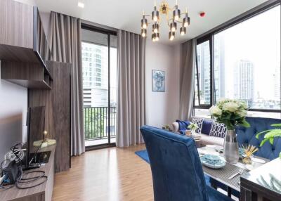 Modern living room with a view of the city, featuring a blue sofa, dining table, and wall-mounted TV