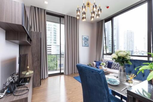 Modern living room with a view of the city, featuring a blue sofa, dining table, and wall-mounted TV