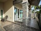 Modern outdoor patio of a building with wicker chairs, a glass table, and stone tile flooring