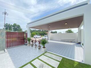 Covered carport area next to a house with potted plants and a grassy area