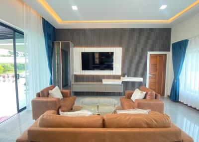 Modern living room with brown sofas, a large TV, and sliding glass doors