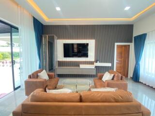 Modern living room with brown sofas, a large TV, and sliding glass doors