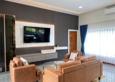 Modern living room with brown leather sofas, wall-mounted TV, and large window