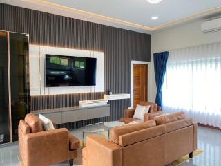 Modern living room with brown leather sofas, wall-mounted TV, and large window