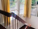 Staircase with wooden steps and metal railings, large windows with curtains, and natural light