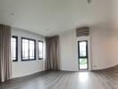 Well-lit empty living room with large windows and wooden flooring