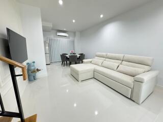 Modern living room with a mounted TV, comfortable gray sectional sofa, dining table, and minimalist decor