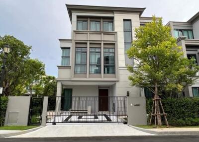 Exterior view of a modern three-story house with trees and a gated entry.