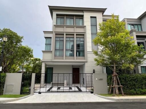 Exterior view of a modern three-story house with trees and a gated entry.