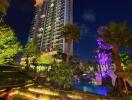 Nighttime view of a tall residential building with illuminated outdoor area and pool