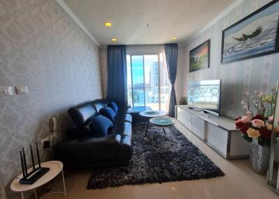 Modern living room with large window, black leather sofa, and TV on white stand.