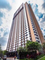 tall residential apartment building with multiple floors and trees at the entrance